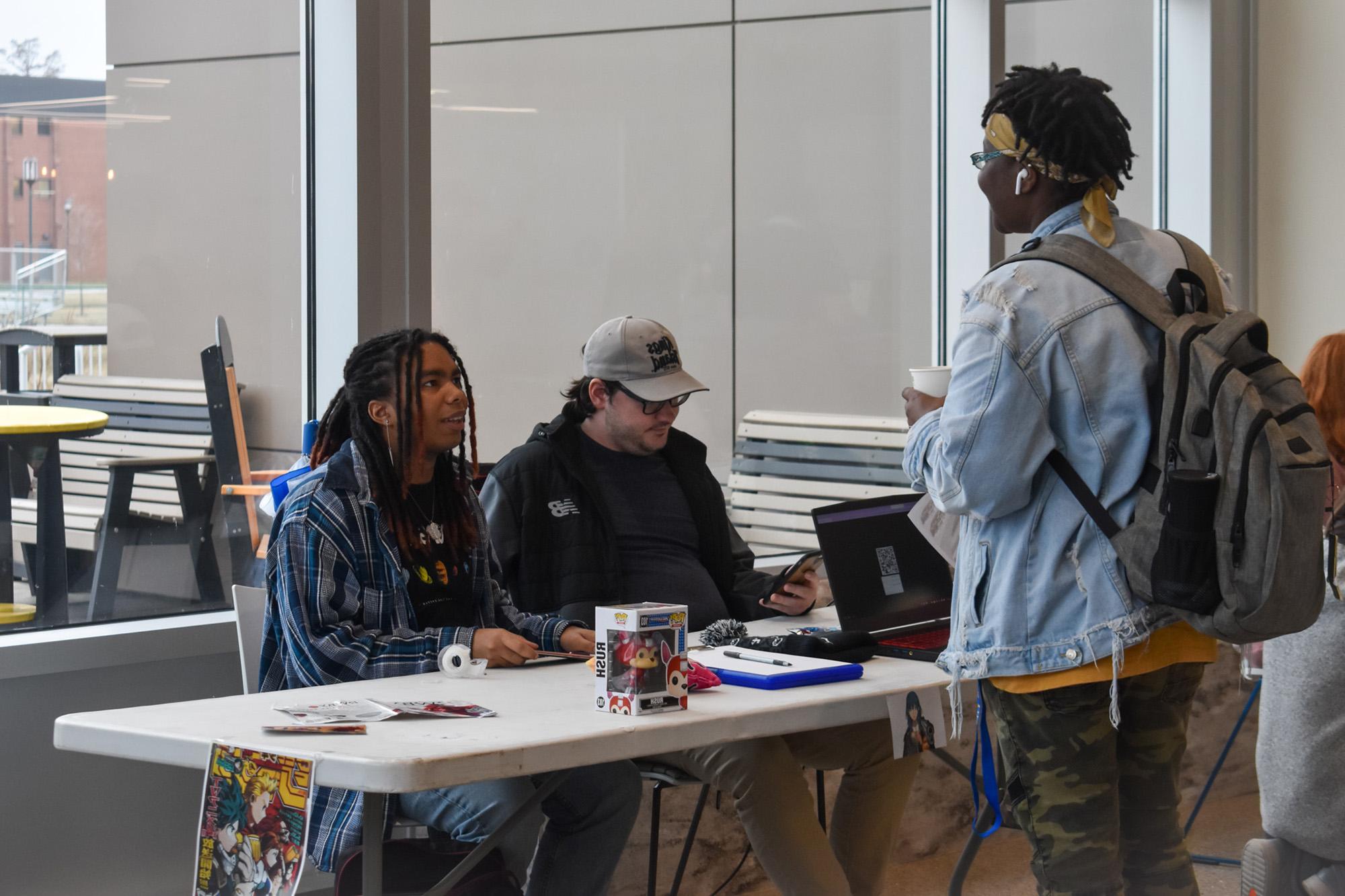 Two students sitting at a table in Jefferson Student Union talking to another student